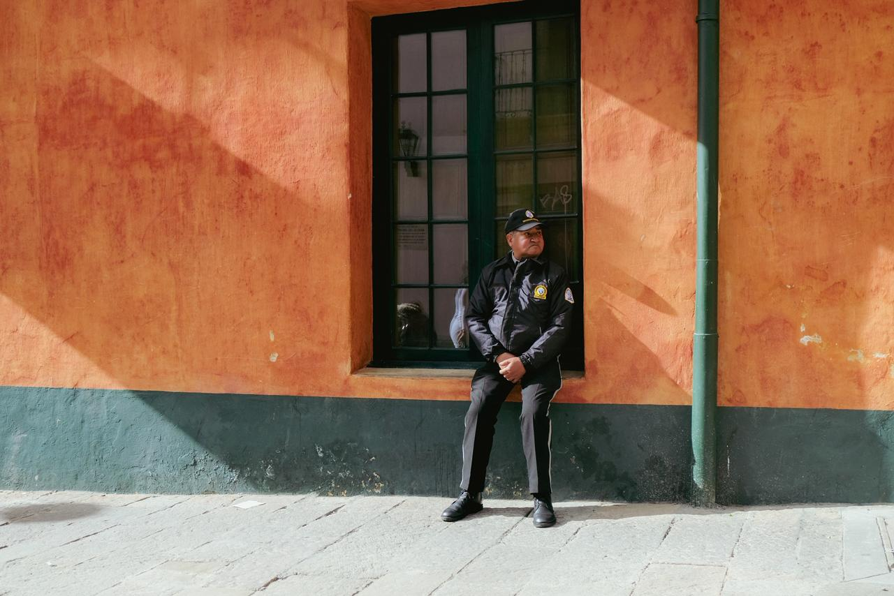 Homem uniformizado sentado na soleira de uma janela em uma parede laranja, olhando para o lado