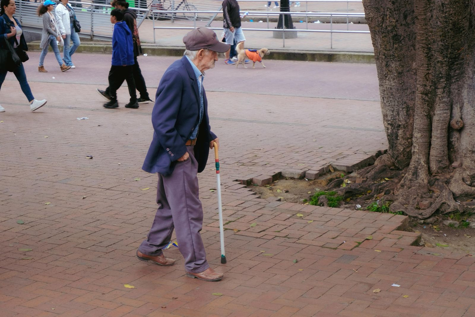 Idoso caminhando com bengala em praça pública